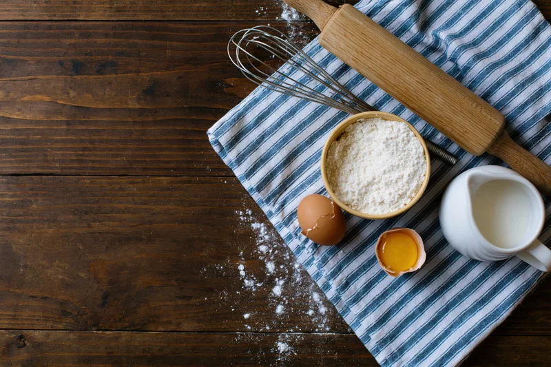 Baking ingredients arranged on a striped cloth over a wooden table with copyspace on the left