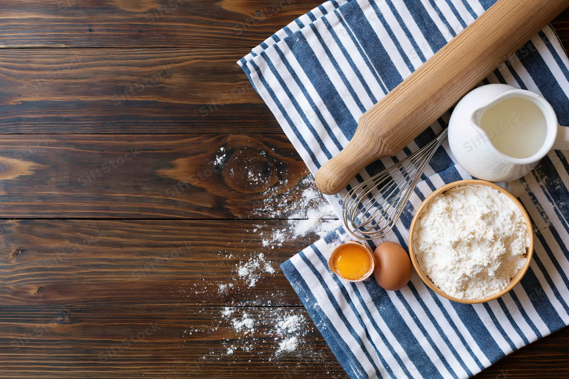 Baking ingredients arranged on a striped cloth over a wooden table with copyspace on the left