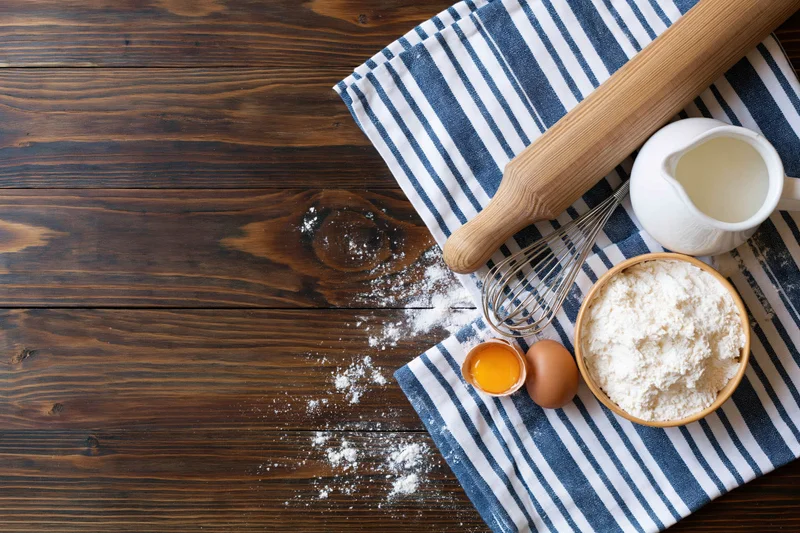 Baking ingredients arranged on a striped cloth over a wooden table with copyspace on the left
