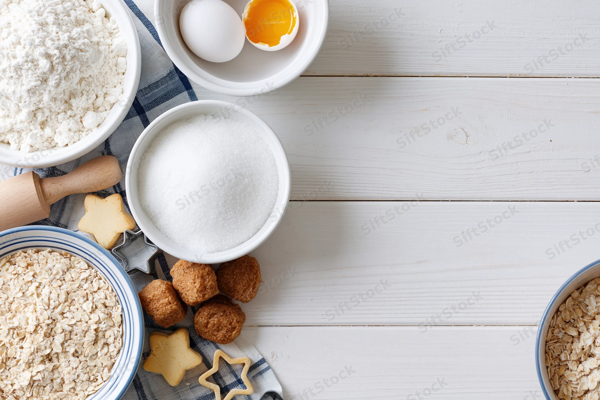 Baking ingredients arranged on a white wooden table with cookie cutters and shaped dough pieces