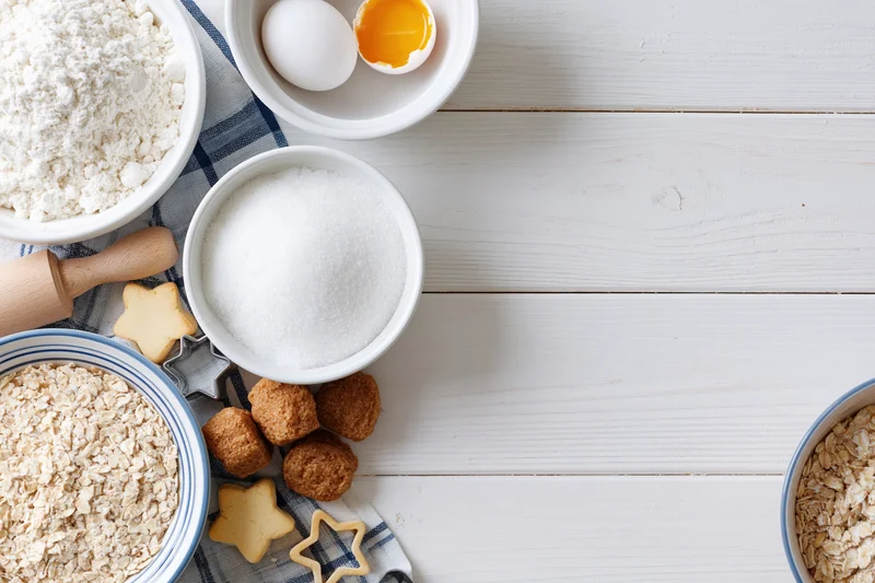 Baking ingredients arranged on a white wooden table with cookie cutters and shaped dough pieces