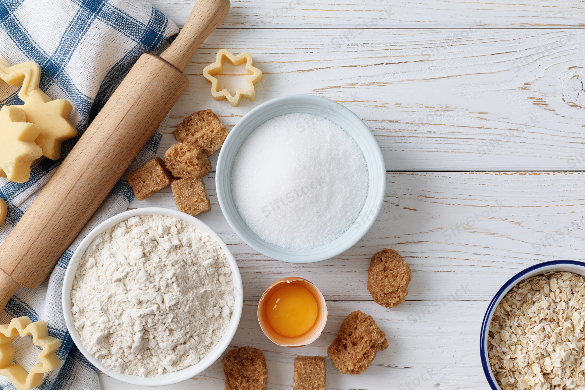 Baking ingredients arranged on a white wooden table with rolling pin and cookie cutters