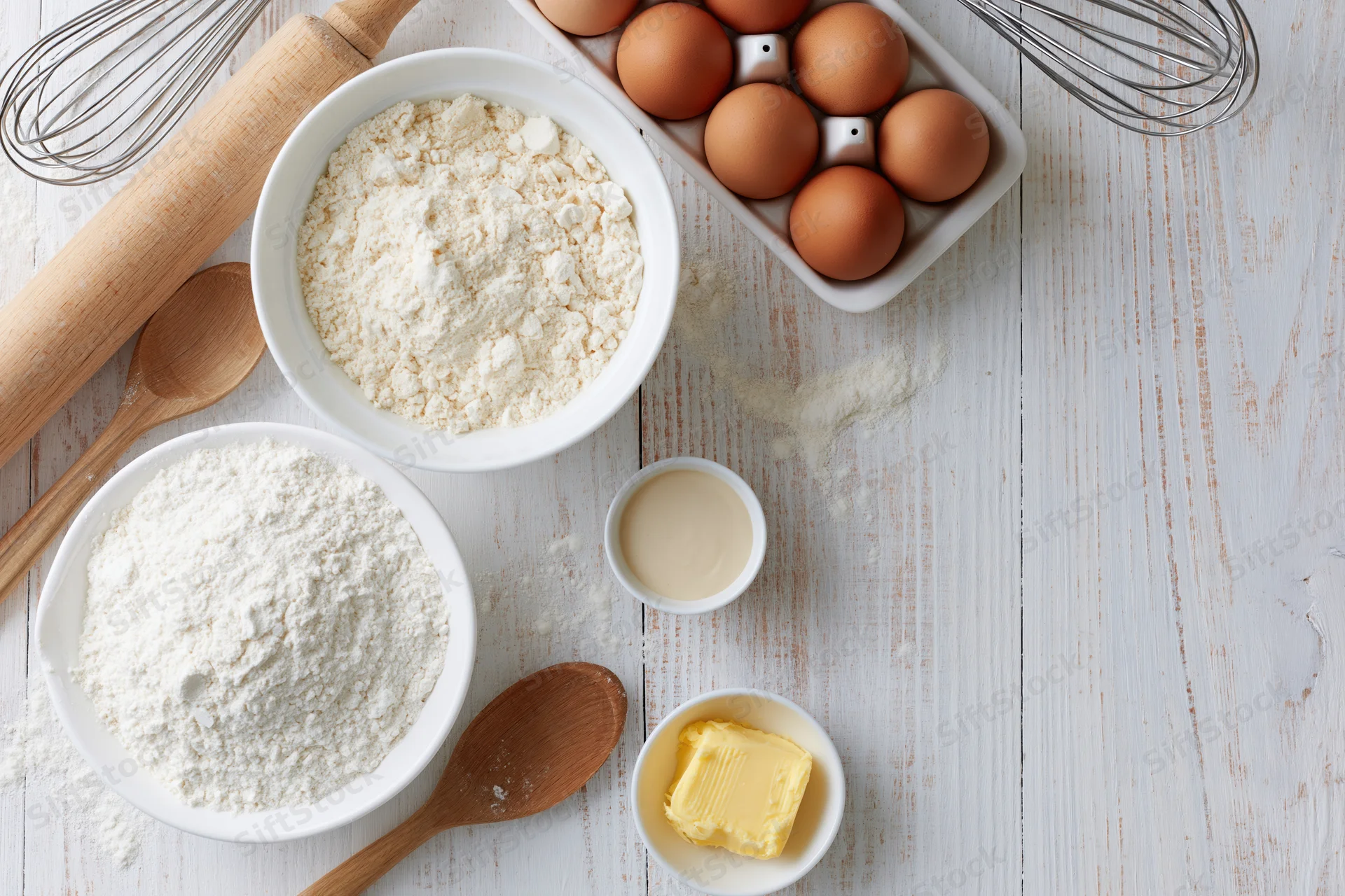 Baking ingredients arranged on a white wooden surface with copyspace