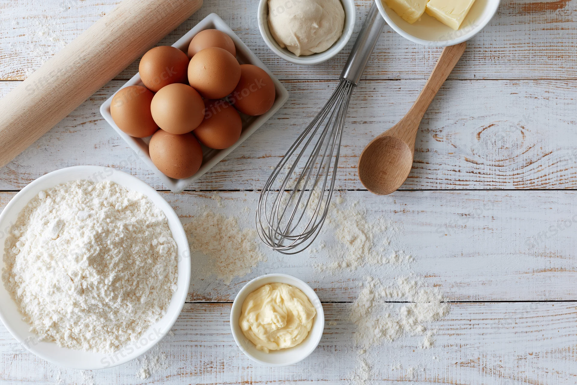 Baking ingredients arranged on a white wooden table with utensils and bowls
