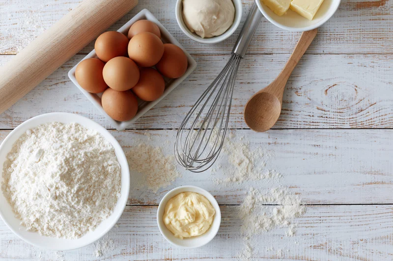 Baking ingredients arranged on a white wooden table with utensils and bowls