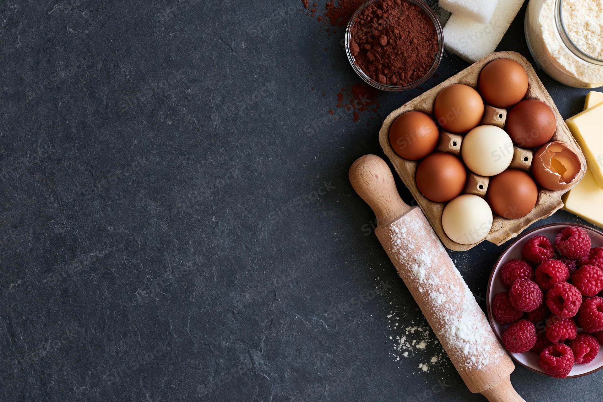 Baking ingredients arranged on dark slate countertop with copyspace
