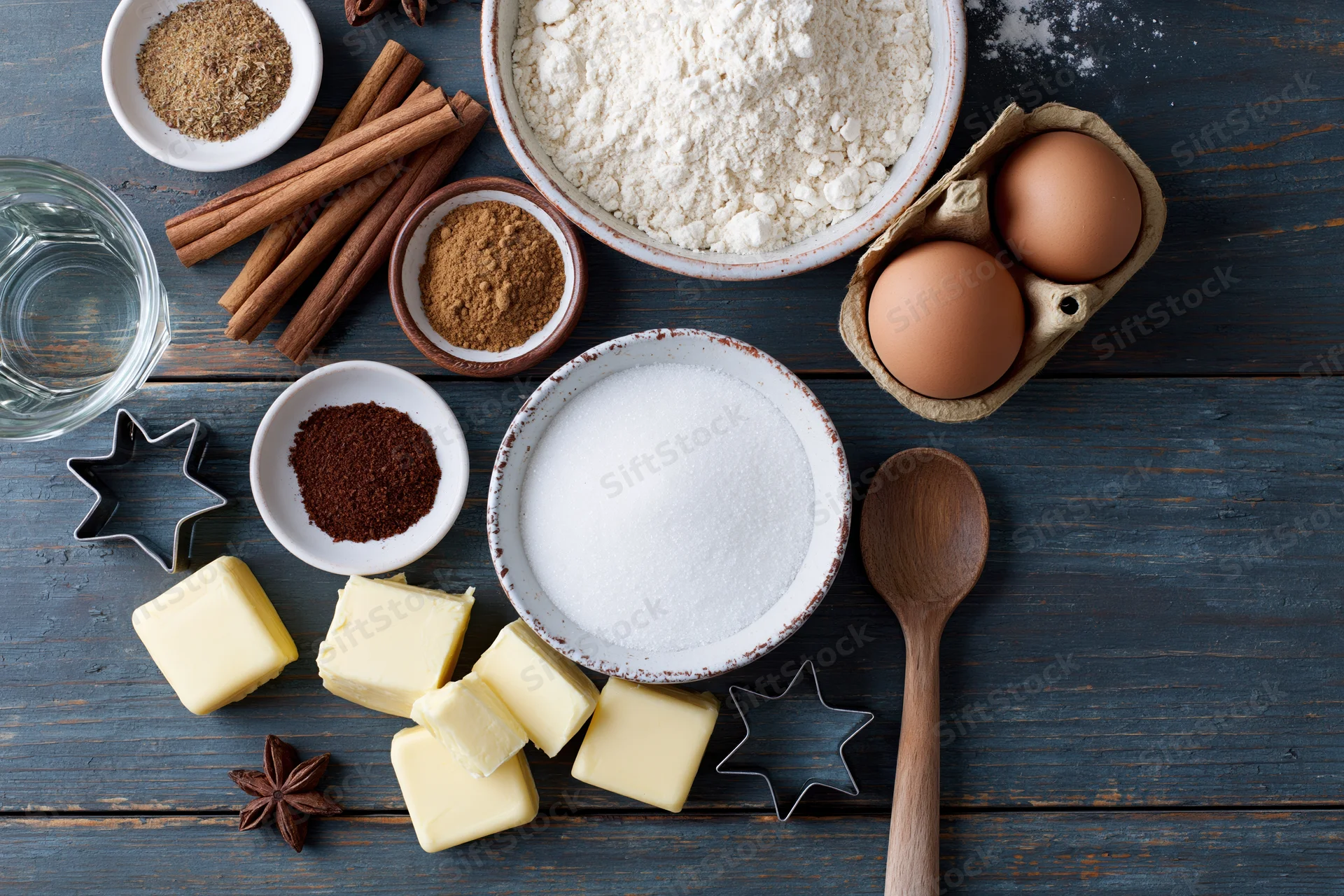 Baking ingredients arranged on a dark wooden table with cookie cutters and utensils