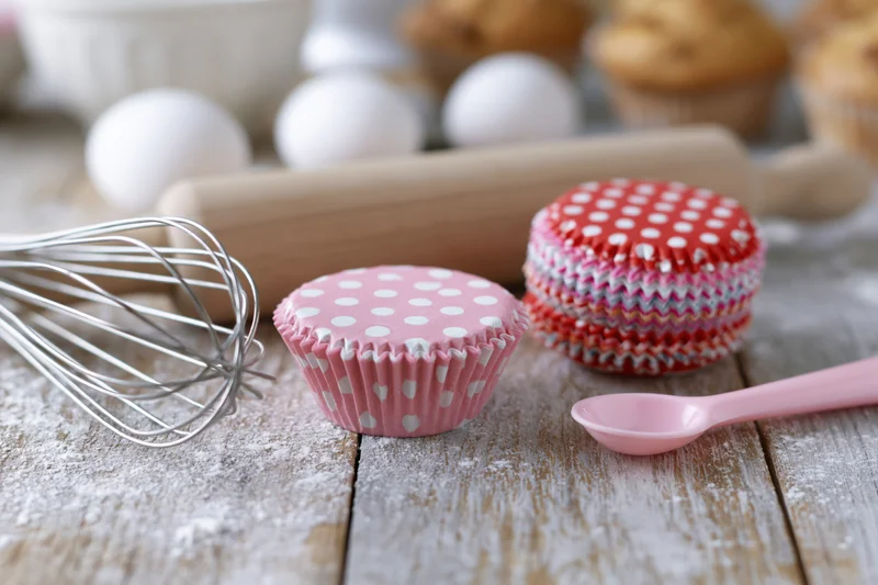 Pink and red polka dot cupcake cases on a floured wooden table with baking tools around