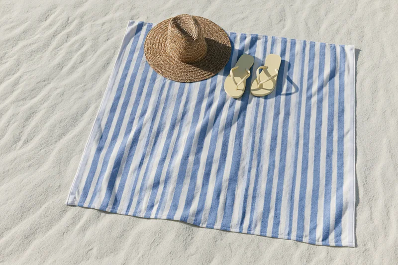 Blue and white striped towel with straw hat and flipflops on sandy beach