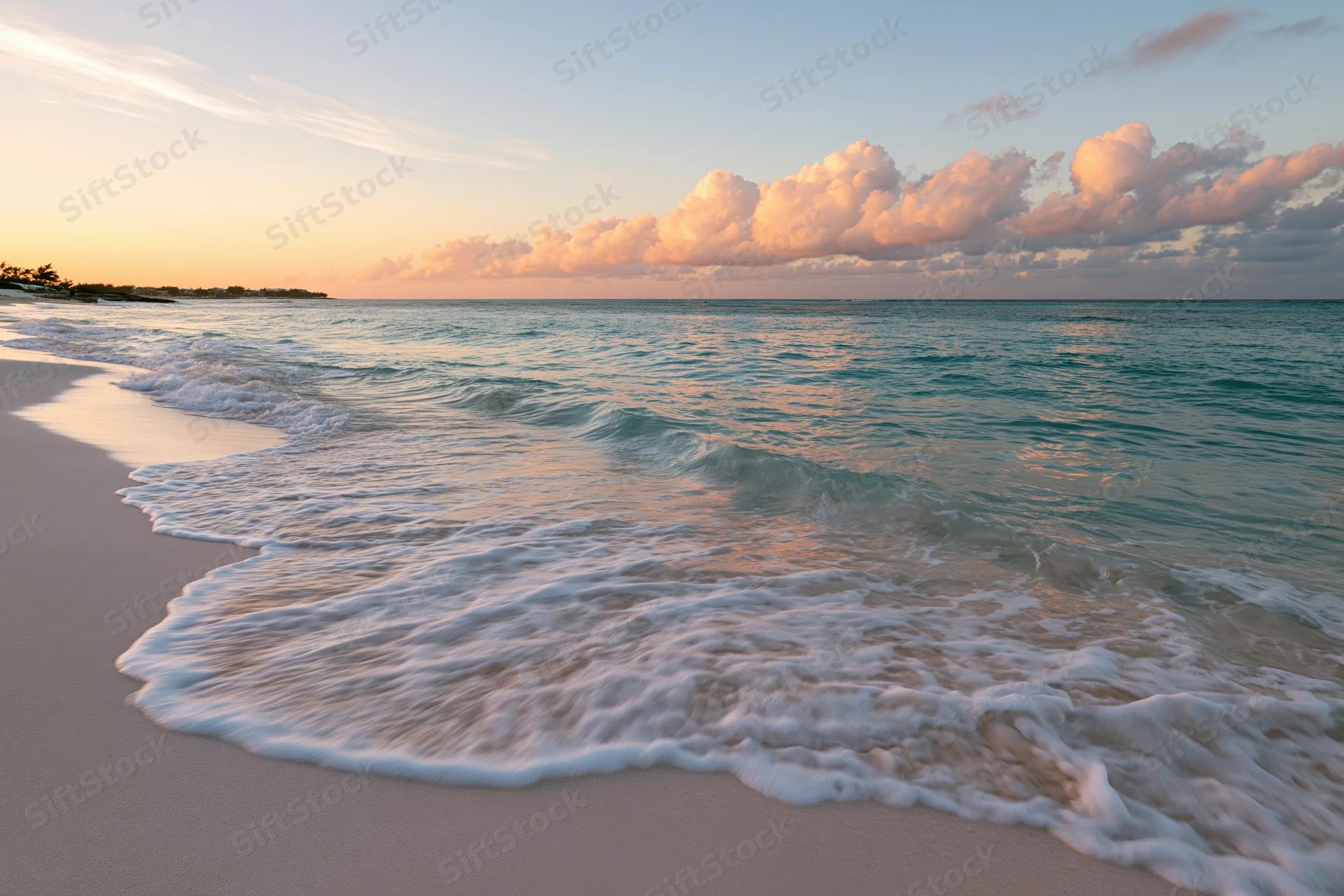 Waves rolling onto a sandy beach at sunset with pink clouds above the ocean horizon