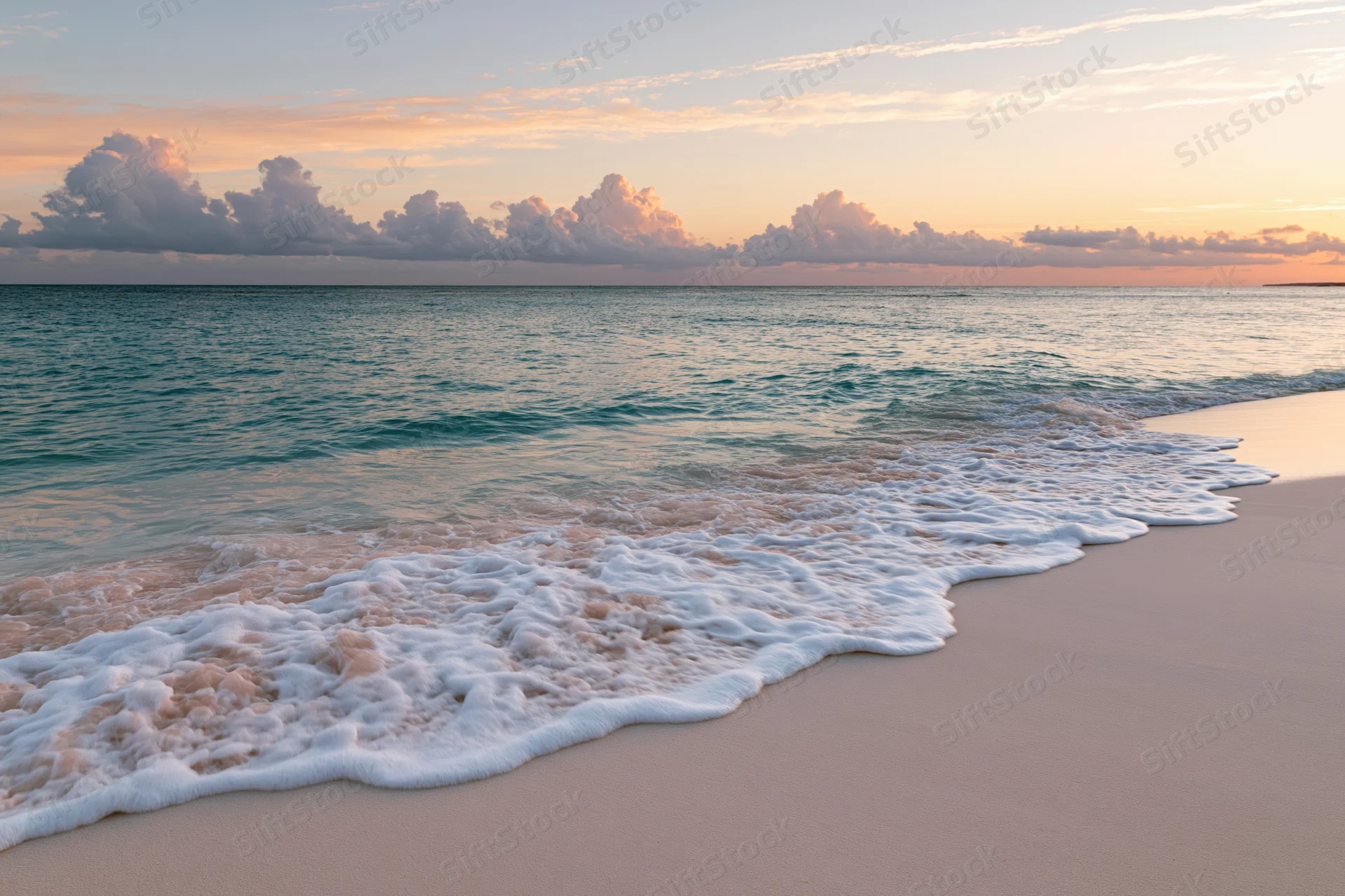 Gentle waves with white foam rolling onto a sandy beach at sunset