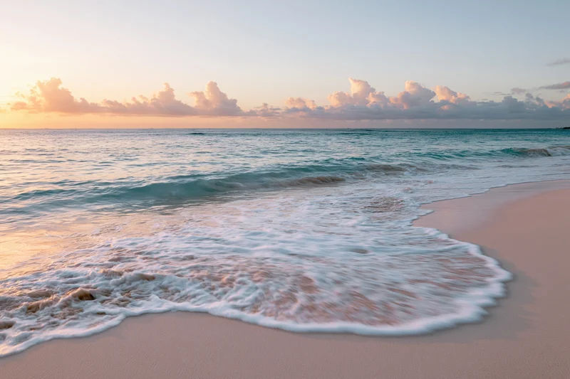Waves rolling onto sandy beach at sunset with clouds above the ocean horizon