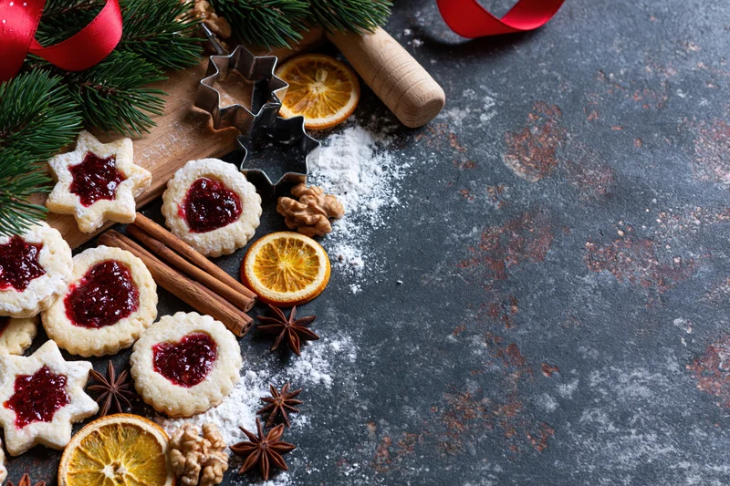 Star and heart shaped cookies with jam, cinnamon, dried orange, walnut and anise on a dark rustic countertop with pine and red ribbon, flat lay view