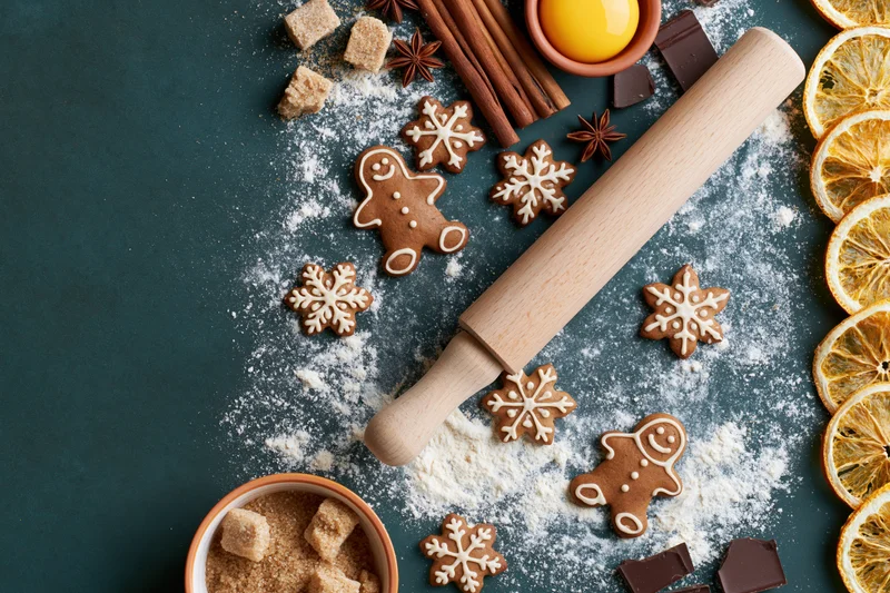 Gingerbread cookies and baking ingredients arranged on a dark surface with flour and dried oranges