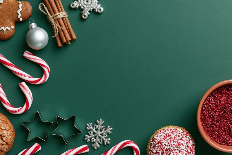 Christmas decorations and baked goods arranged along the edges of a green surface with copyspace in the center
