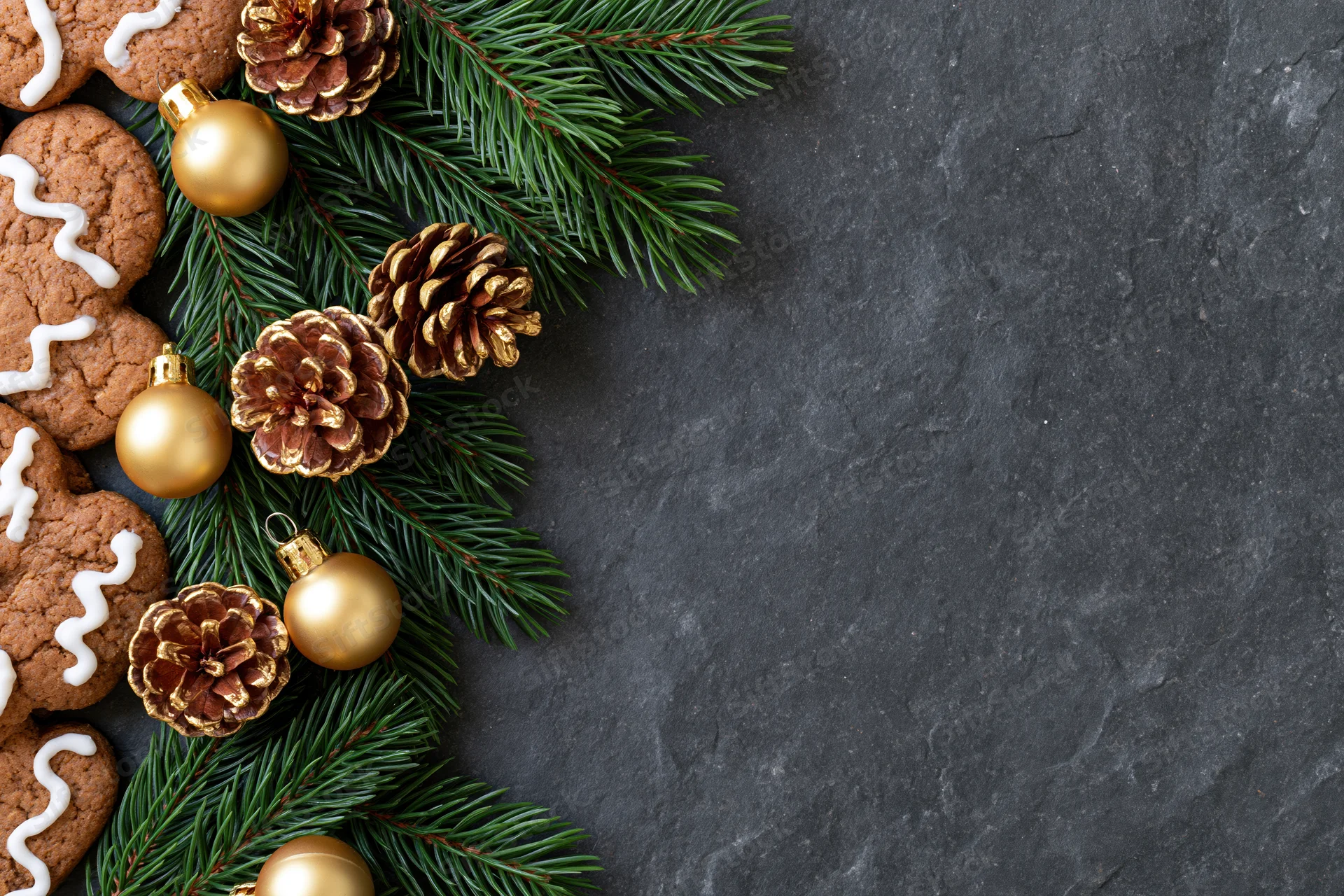 Christmas decorations and gingerbread cookies arranged on dark stone surface with copyspace