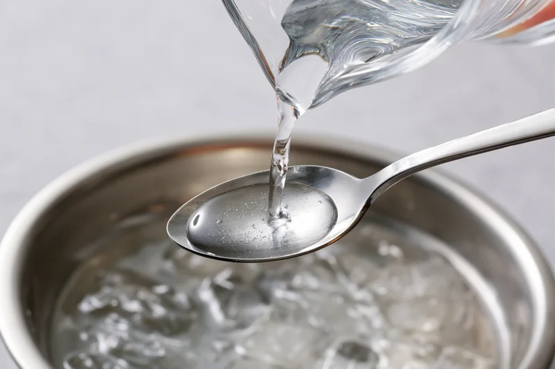 Water being poured from a glass pitcher onto a spoon over a metal bowl