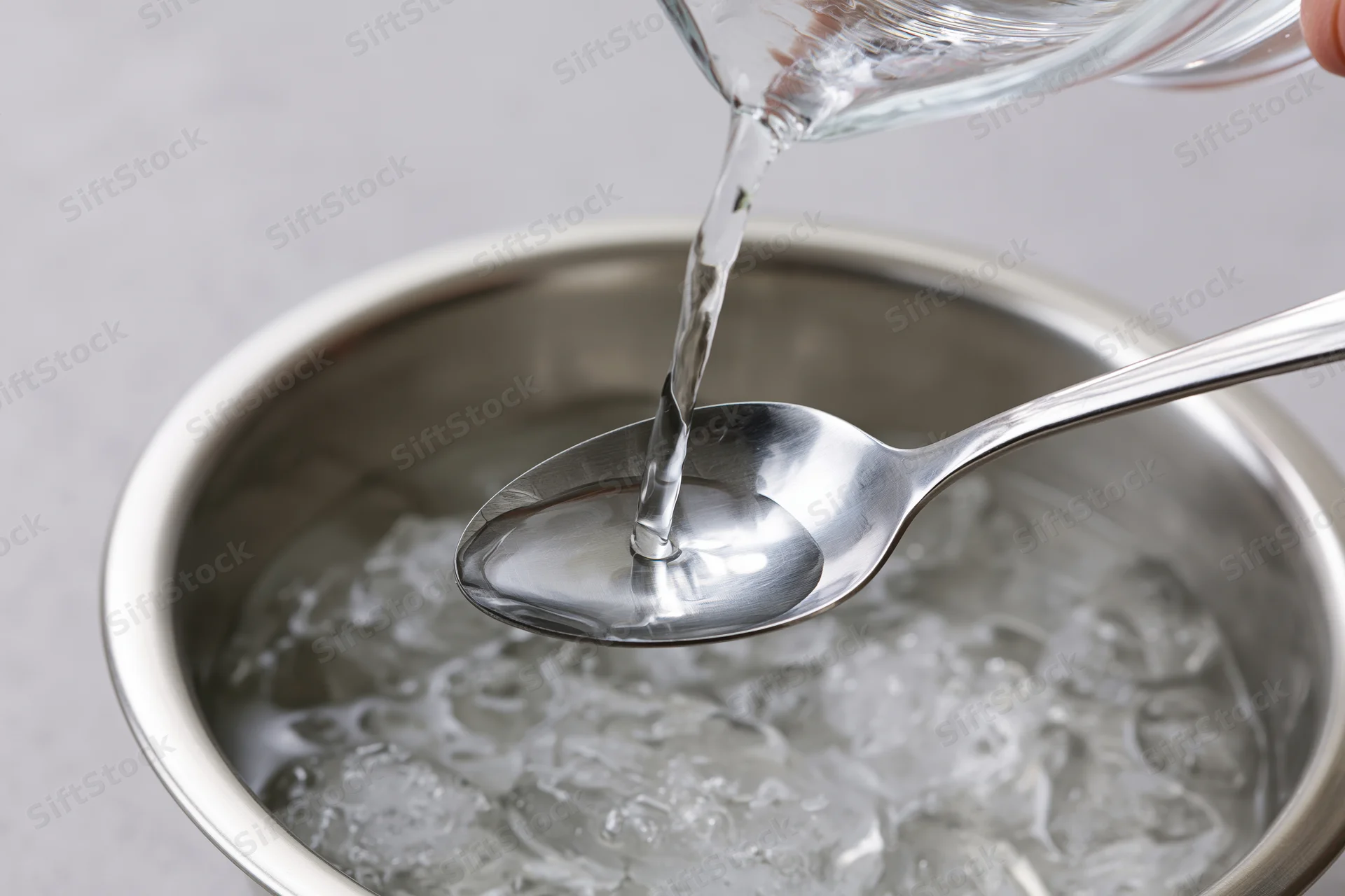 Water being poured from a glass into a spoon over a stainless steel bowl