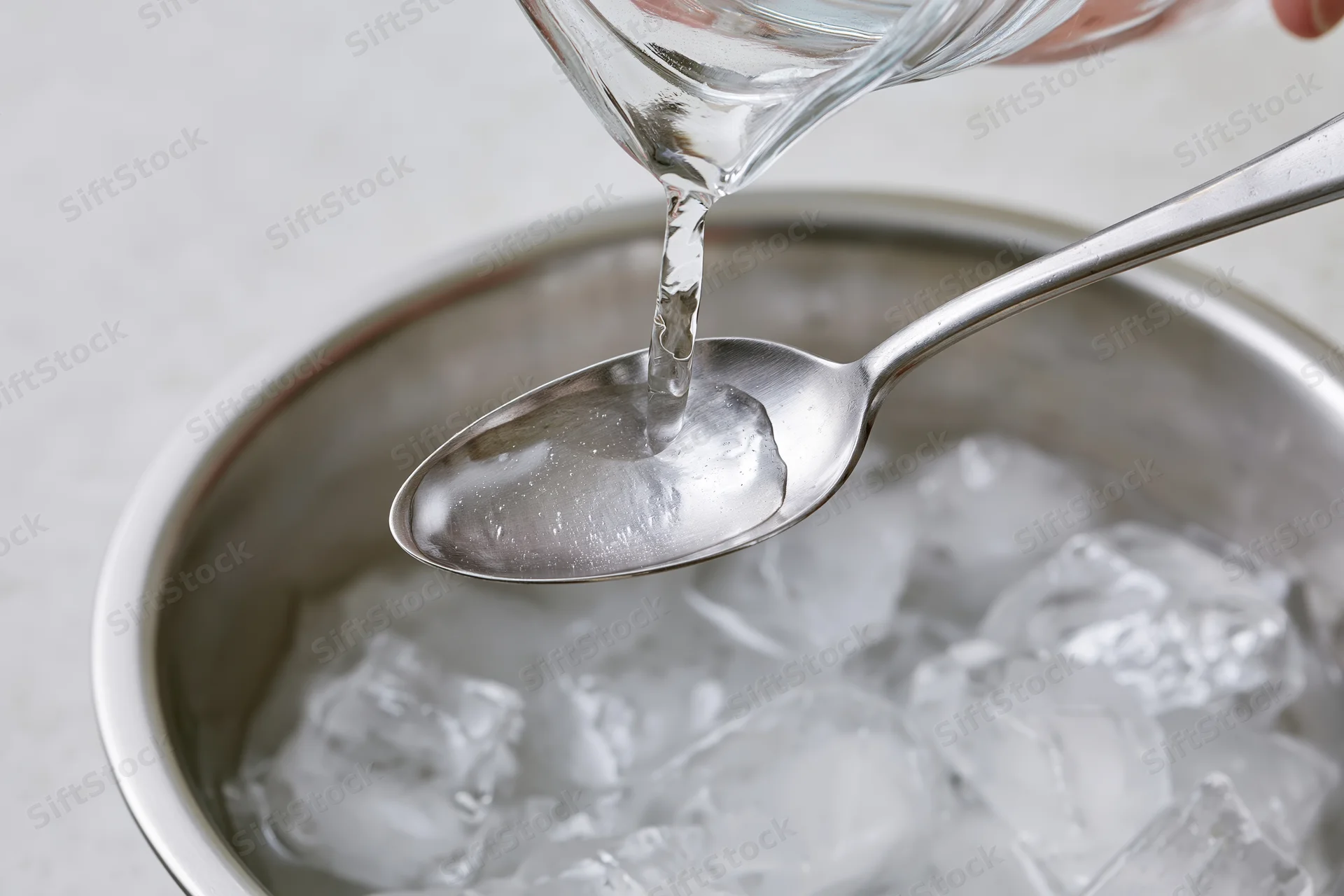 Water being poured from a glass pitcher onto a spoon over a bowl of ice