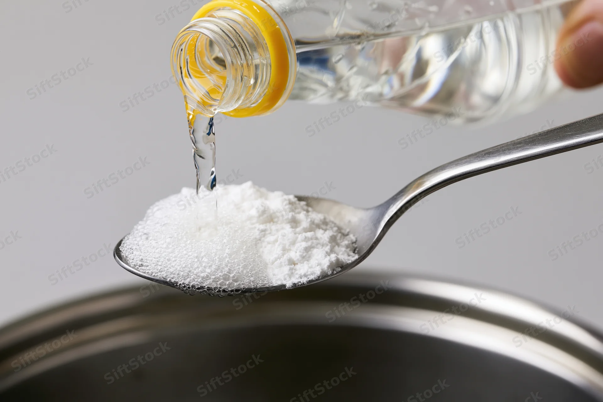 Liquid being poured onto baking powder on a spoon above a pot