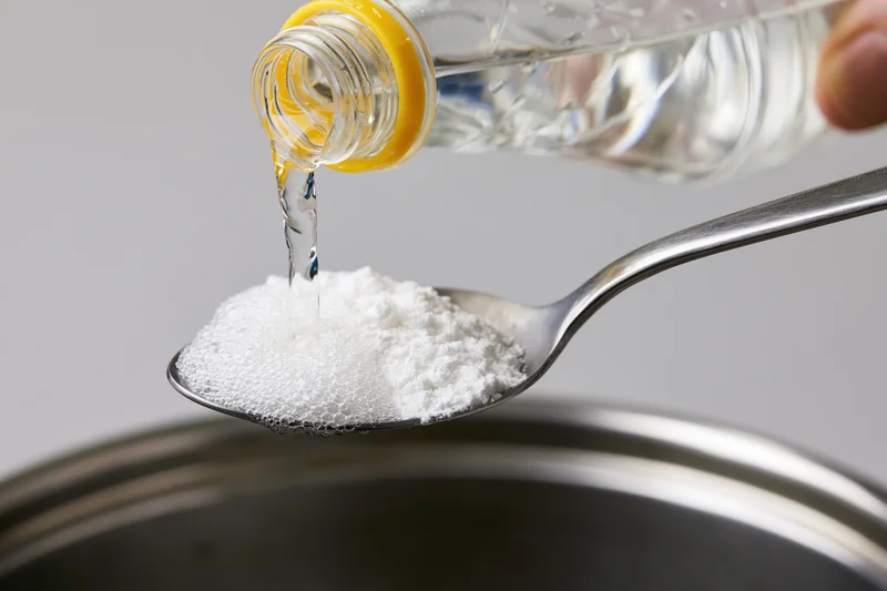 Liquid being poured onto baking powder on a spoon above a pot