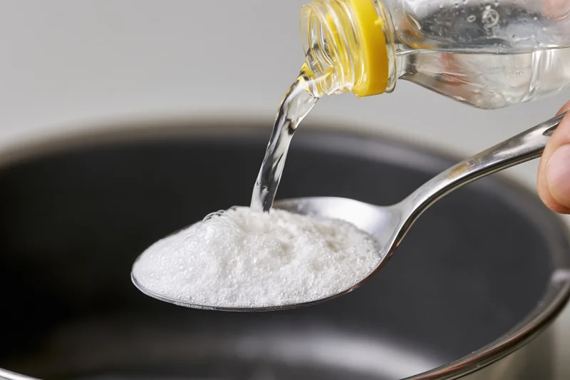 Vinegar being poured onto a spoonful of white powder over a pot
