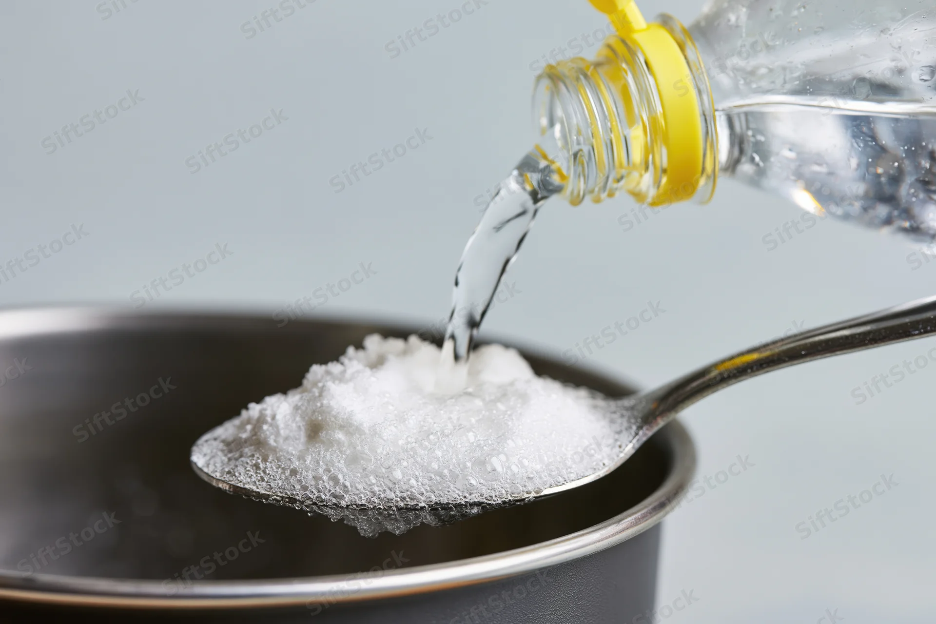 Vinegar being poured onto a spoonful of white powder in a metal bowl