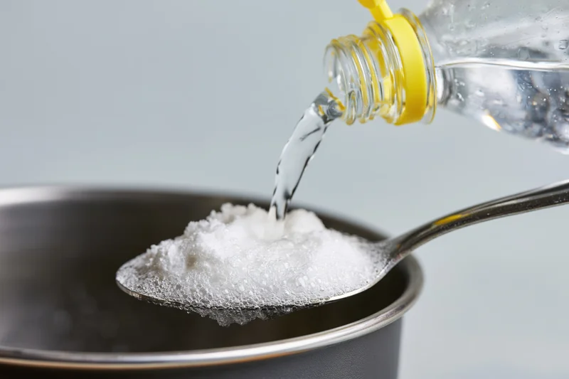 Vinegar being poured onto a spoonful of white powder in a metal bowl