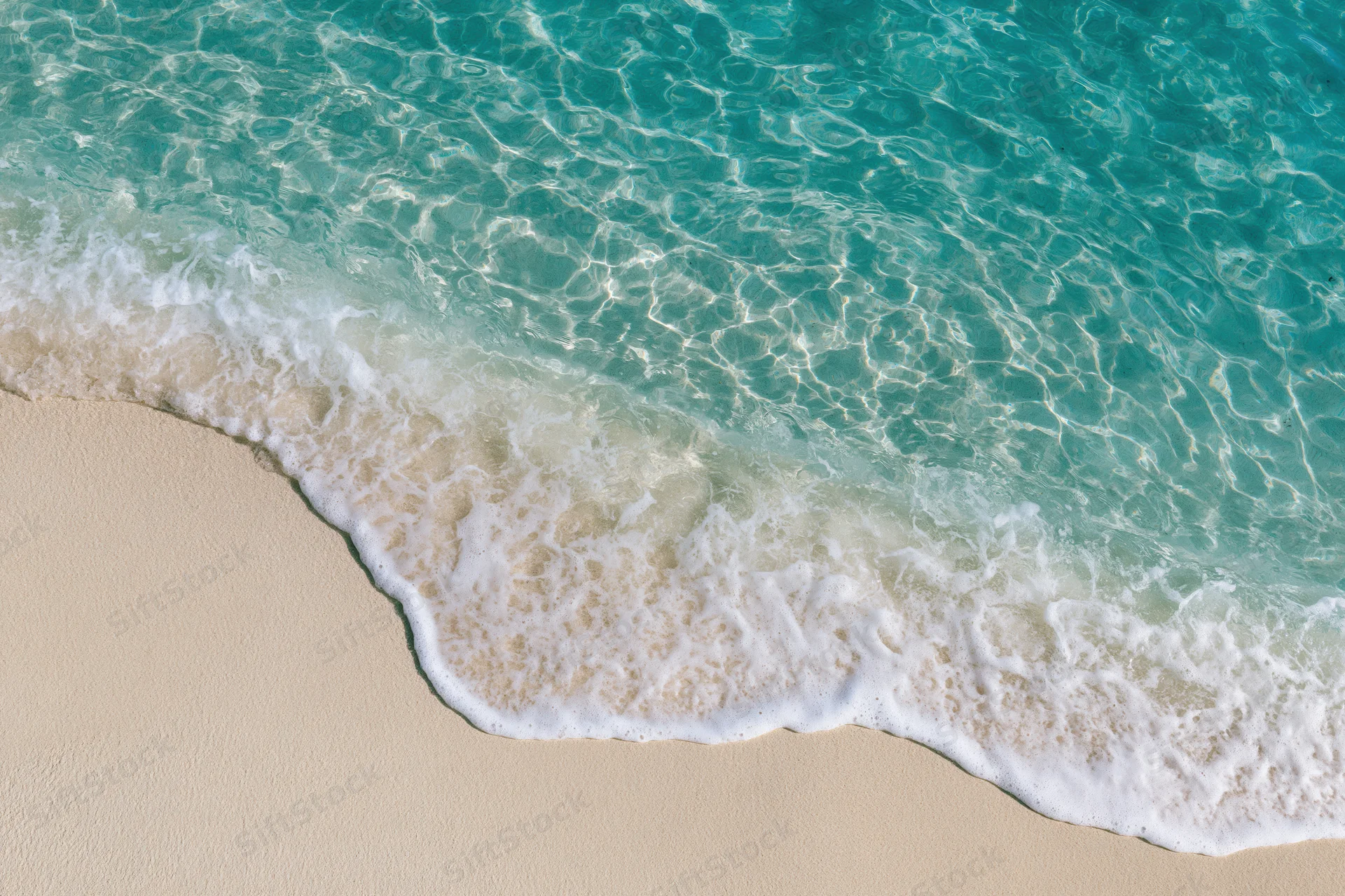 Turquoise ocean wave breaking onto sandy beach from above