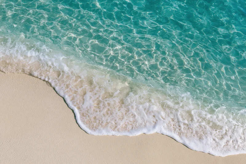 Turquoise ocean wave breaking onto sandy beach from above