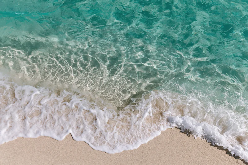 Waves breaking on sandy beach with white foam and turquoise water