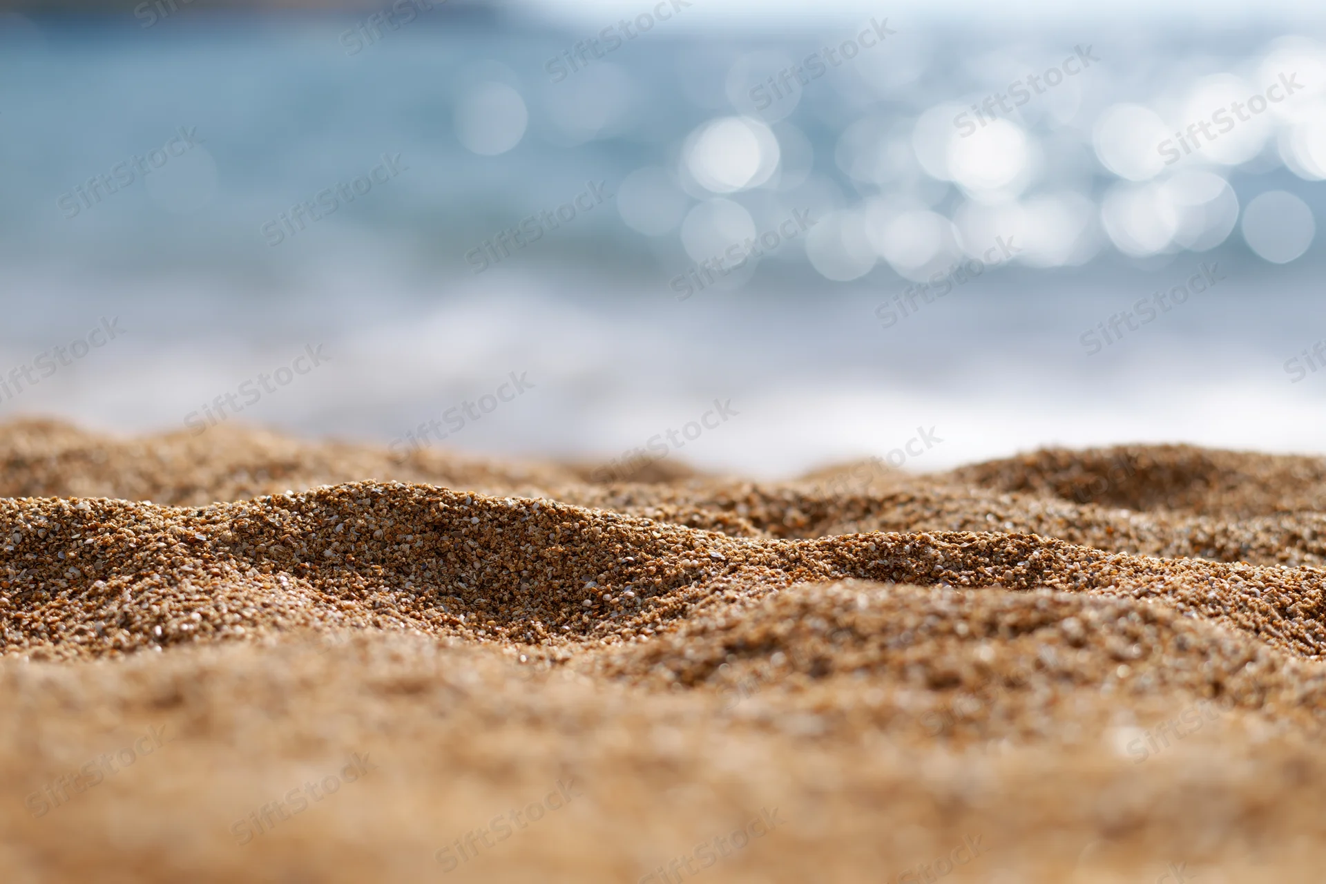 Closeup of textured sand on a beach with blurred ocean waves in the background