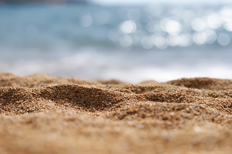 Closeup of textured sand on a beach with blurred ocean waves in the background