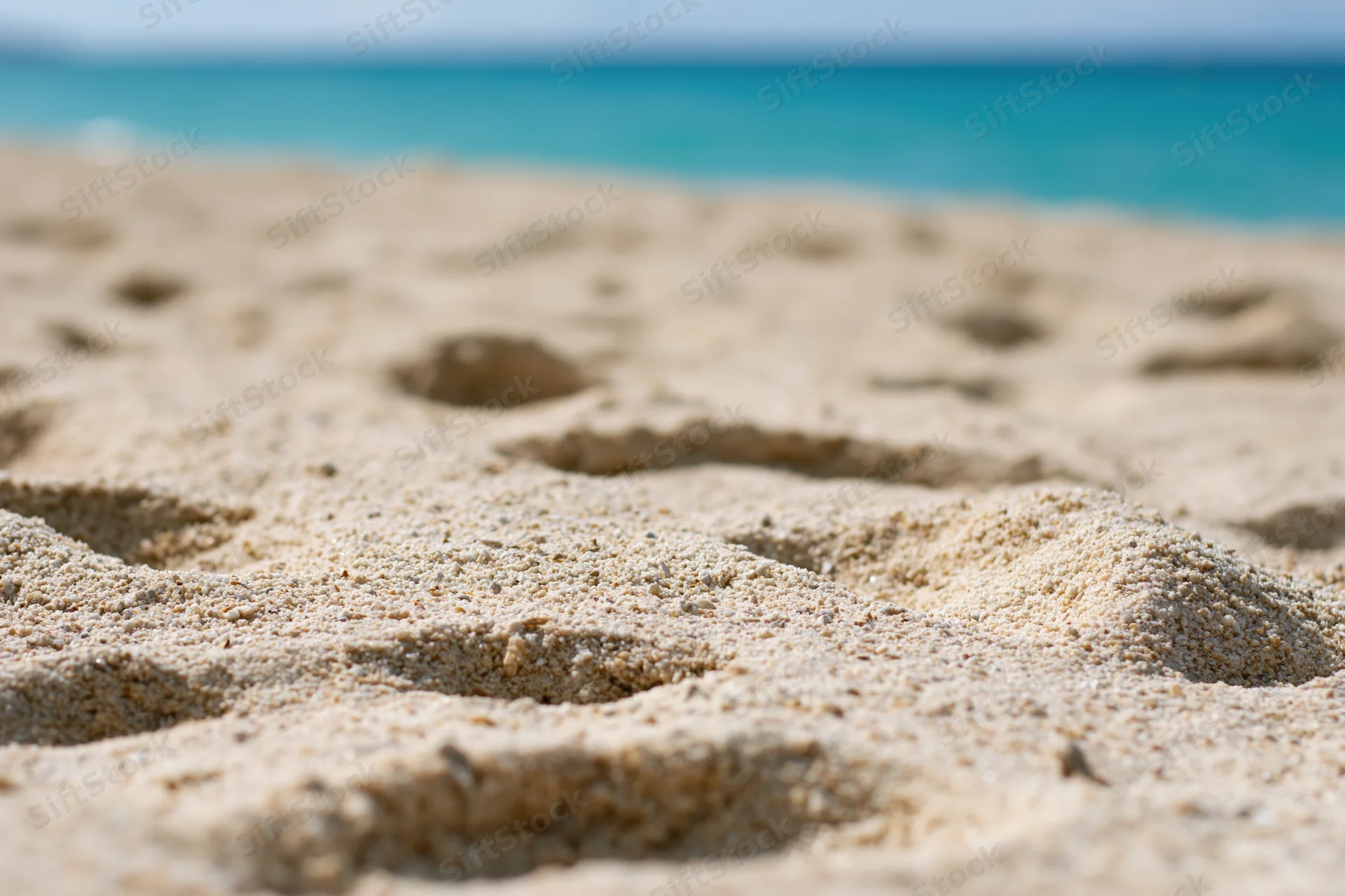 Footprints in the sand along a turquoise ocean shoreline