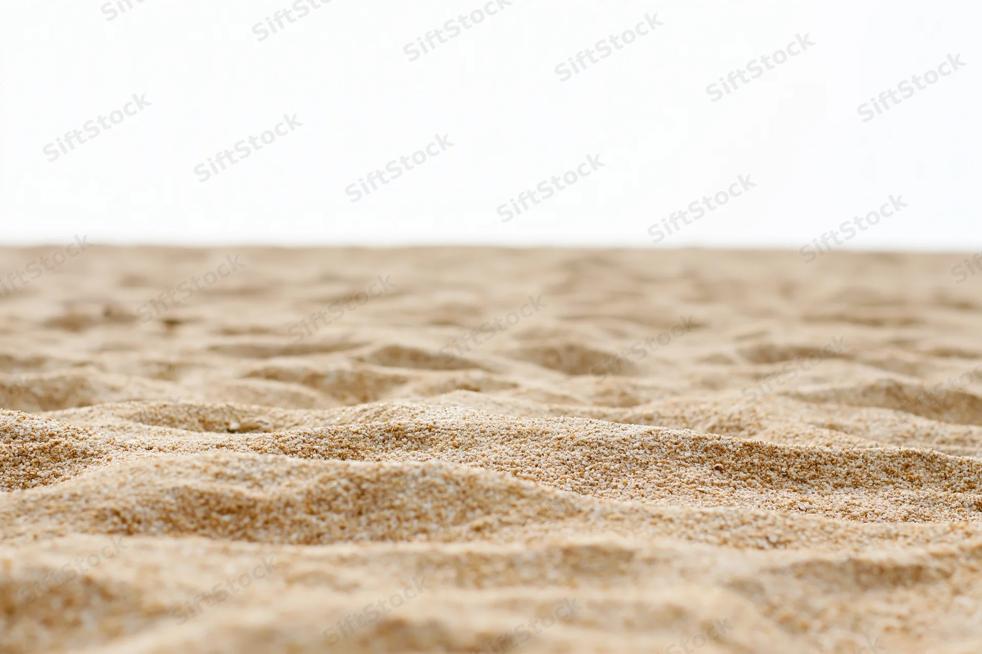 Closeup of textured sand surface with ripples and granular detail against white background
