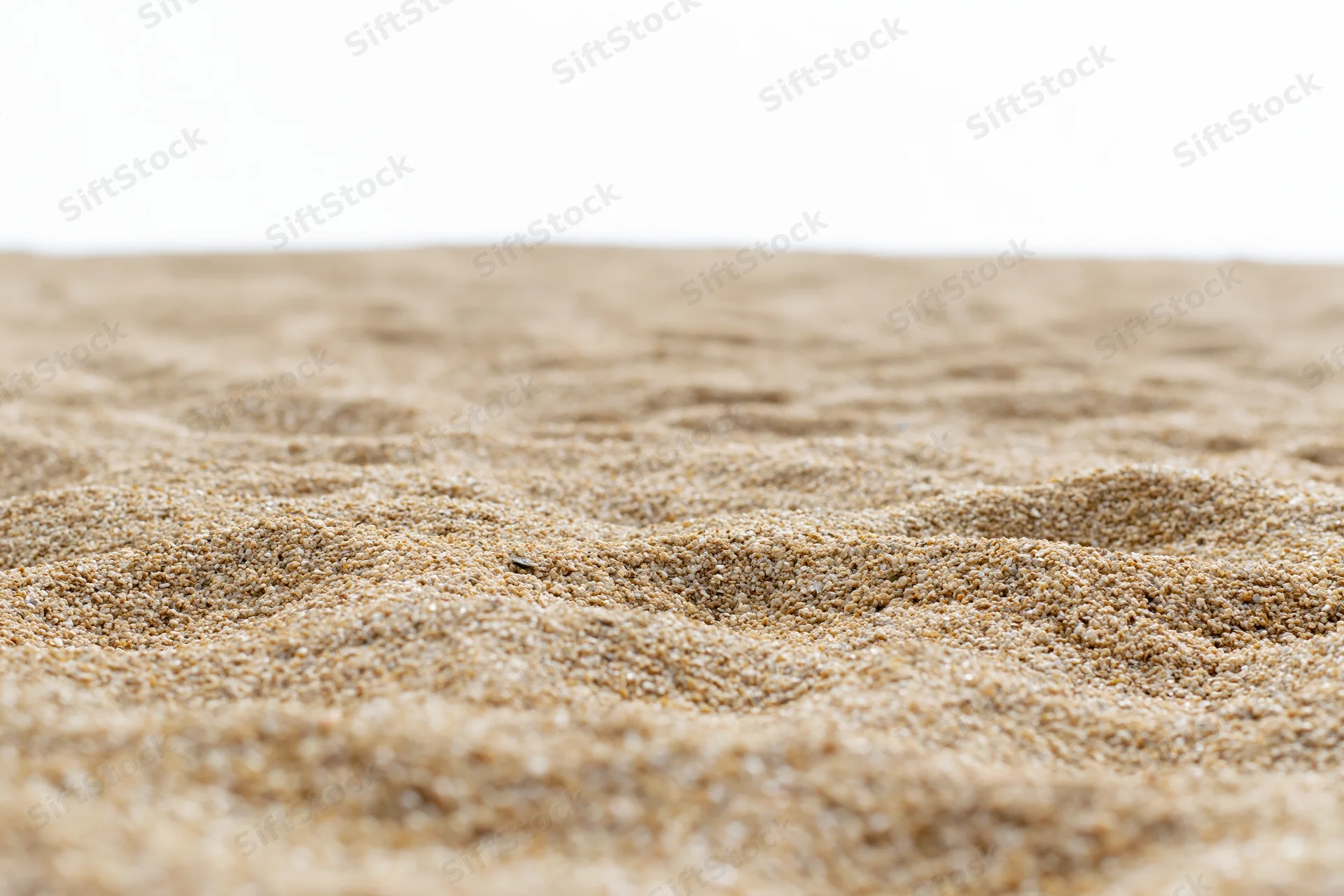 Closeup of textured sand surface with ripples and fine grains on white background