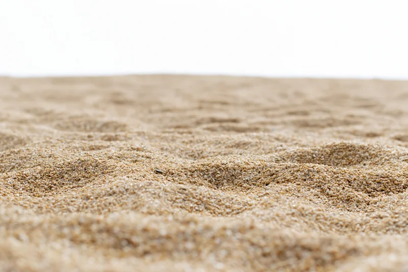 Closeup of textured sand surface with ripples and fine grains on white background