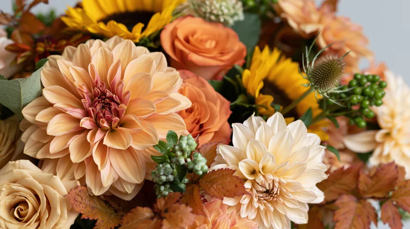 Closeup of a floral bouquet with dahlias, roses, sunflowers, and autumn foliage arranged as a centerpiece