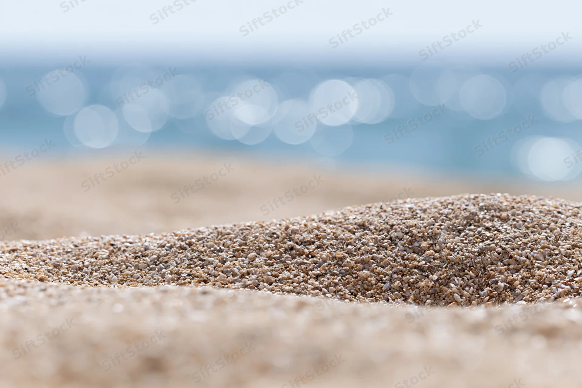 Closeup of textured sand on a beach with blurred ocean and bokeh lights in the background
