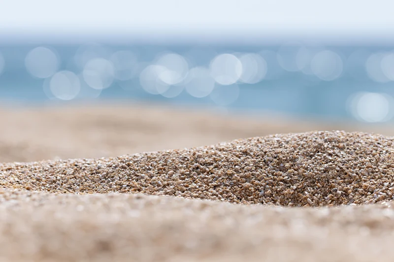 Closeup of textured sand on a beach with blurred ocean and bokeh lights in the background