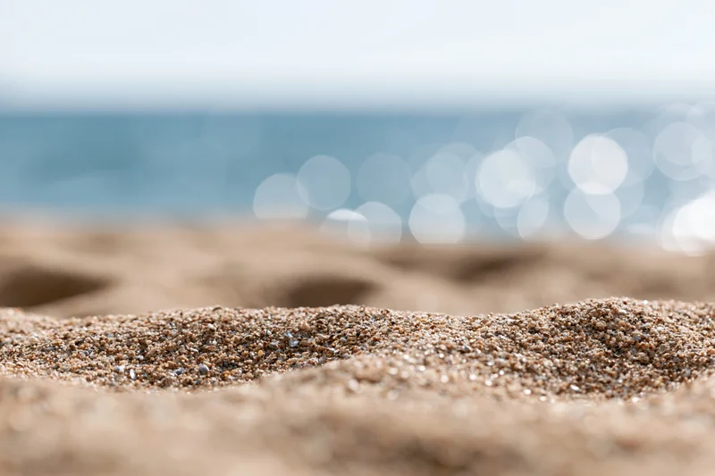 Closeup of textured sand on a beach with blurred ocean and bokeh lights in the background