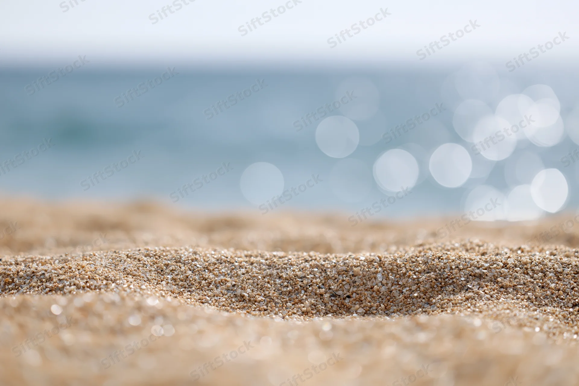 Closeup of textured sand on a beach with blurred ocean and bokeh lights in the background