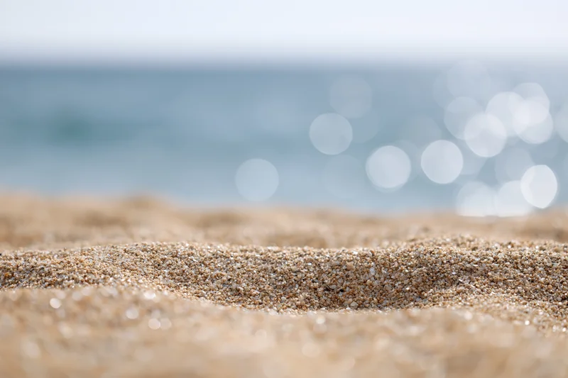 Closeup of textured sand on a beach with blurred ocean and bokeh lights in the background