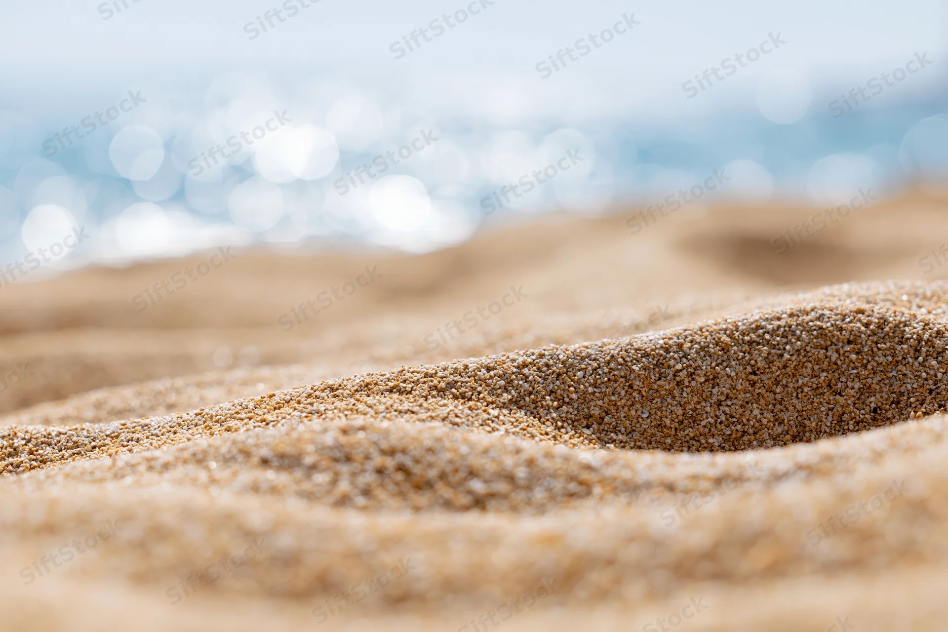 Closeup of textured sand on a beach with blurred ocean in the background