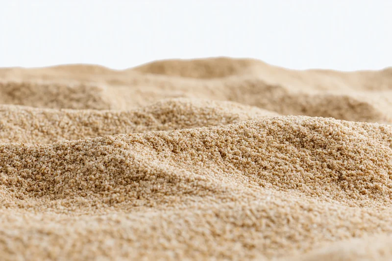 Closeup of textured sand surface with fine granules forming undulating patterns against white background