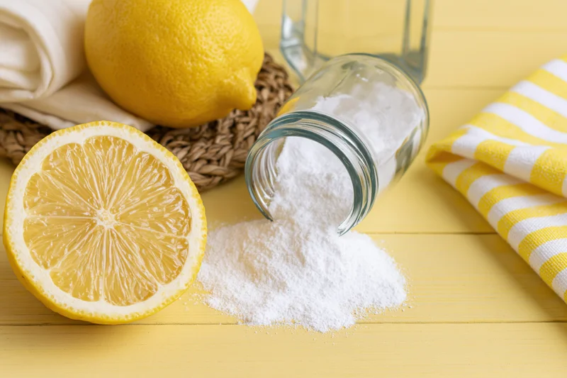 Lemon halves and spilled white powder from a glass jar on a yellow wooden surface with striped towel and woven basket