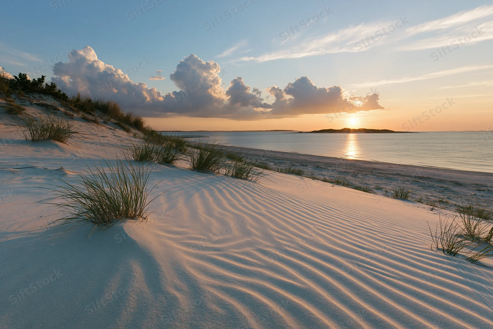Sunset over sandy dunes with ocean and clouds in the background
