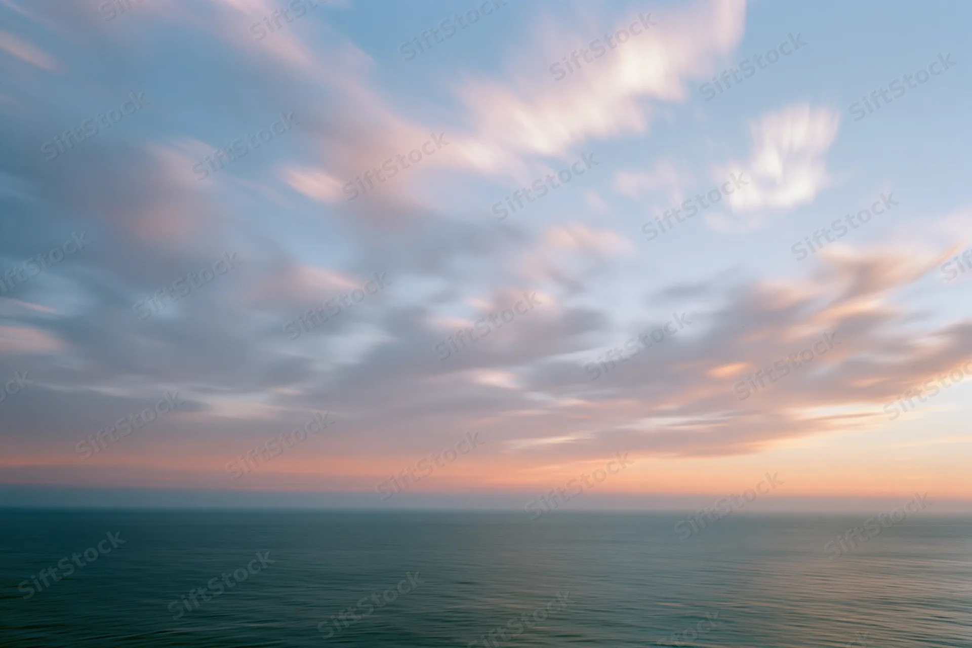 Soft pastel clouds over calm ocean at twilight horizon