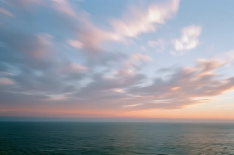 Soft pastel clouds over calm ocean at twilight horizon