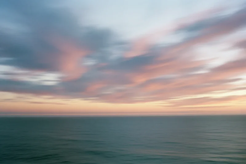 Soft pastel clouds over calm ocean at twilight horizon